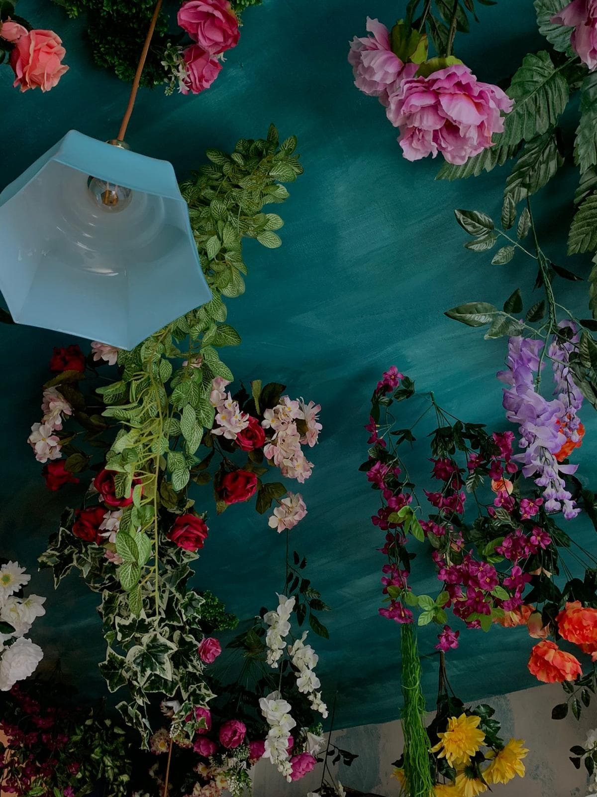 Una lampada azzurra appesa fra le rose e i glicini del soffitto.